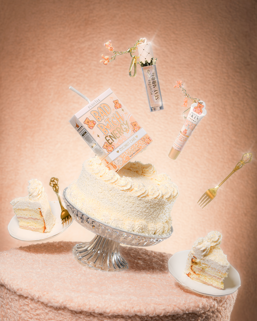 Un gâteau sur une table en tissu peluche avec un duo pour les lèvres P.Louise Teddy Glitter Bad Bitch Energy dans un gâteau à la noix de coco contenant un revitalisant pour les lèvres et de l'huile pour les lèvres flottant autour du gâteau