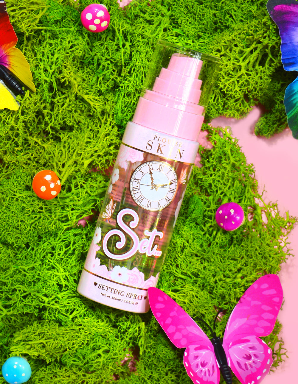 Une bouteille de spray fixateur longue durée P. Louise Ready Set Slay entourée d'éléments décoratifs, notamment de fausses mousses colorées, de papillons et de champignons.