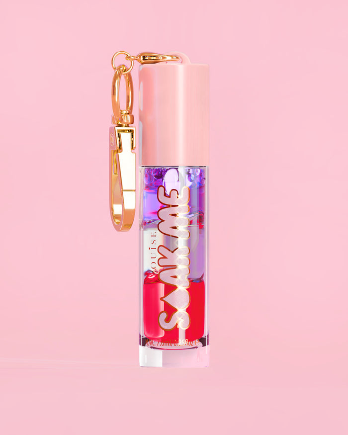 P. Louise Soak Me Lip Oil avec de l'huile en couches colorées dans un tube rose avec un fermoir doré sur fond rose