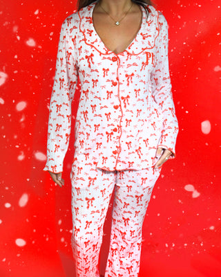 Shot of a womans body wearing a festive set of pink and white striped pyjamas with red bow designs on them against a red background and snowflakes