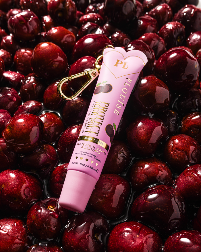 Revitalisant à lèvres teinté rose parfum cerise noire pour protéger votre moue avec clip doré sur un lit de cerises