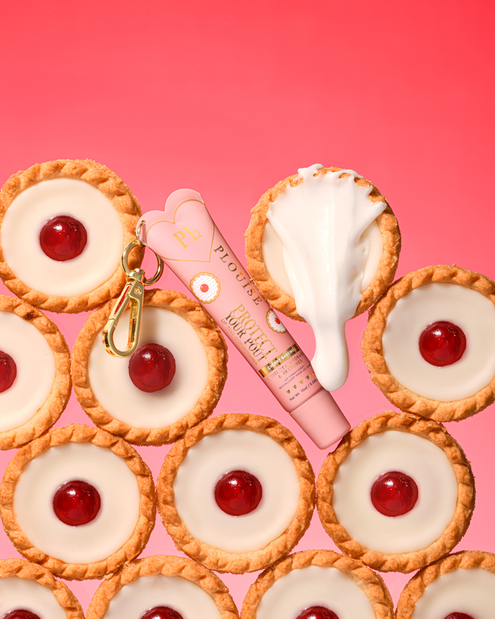 Revitalisant à lèvres teinté au parfum de cerise et d'amande rose pour protéger votre moue avec un clip doré placé entre les desserts à la cerise