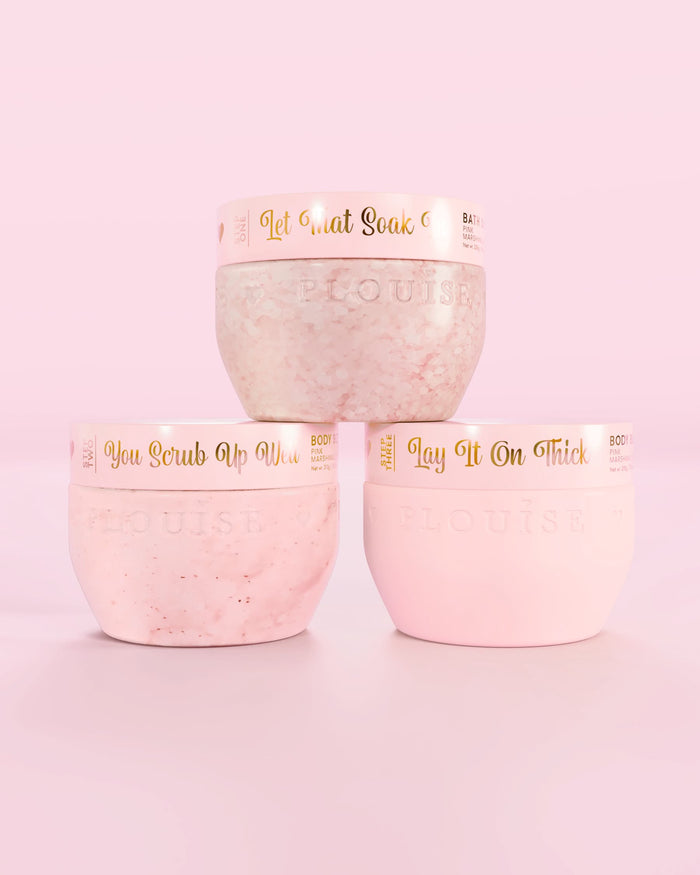 Trois contenants roses P.Louise Hop Into Self-Care Pink Marshmallow contenant des sels de bain, un gommage corporel et du beurre corporel avec un texte doré sur fond rose