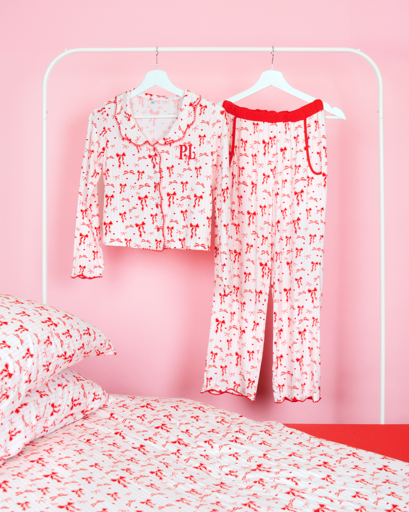 Ensemble de pantalon de pyjama à nœud de Noël P.Louise pour filles, avec un motif à nœud rouge sur l'ensemble des rayures roses et blanches accroché à des cintres dans une chambre rose avec literie assortie