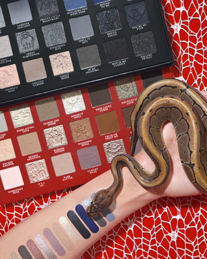 Palette de fards à paupières et de maquillage d'Halloween P.Louise Mystic Moonlight avec des échantillons sur un bras avec un serpent enroulé autour sur un fond de toile d'araignée rouge