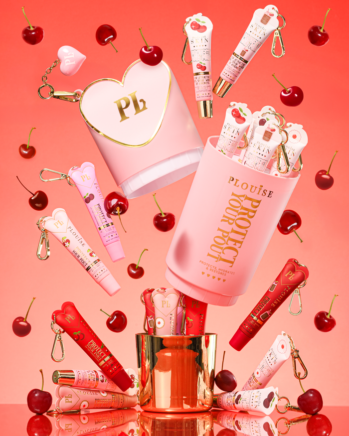 Coffret cadeau Pink XL Protect Your Pout ouvert entouré de cerises et de revitalisants à lèvres roses et rouges sur fond rose