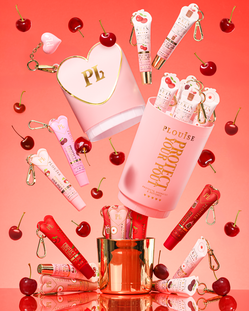 Coffret cadeau Pink XL Protect Your Pout ouvert entouré de cerises et de revitalisants à lèvres roses et rouges sur fond rose