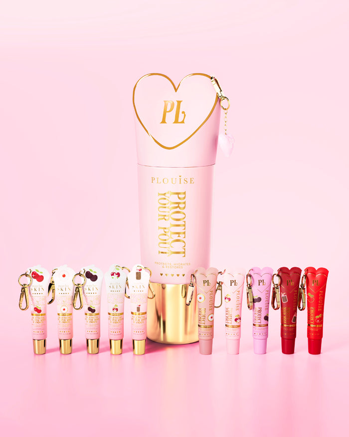 Un ensemble de revitalisants à lèvres parfumés à la cerise rose et rouge avec un rose et un or proéminents protègent votre flacon à moue au centre sur un fond rose.