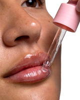 Close-up of a person's lips receiving a clear liquid from a pink P.Louise Lip Loyalty Lip Serum dropper applicator, shown against a white background.
