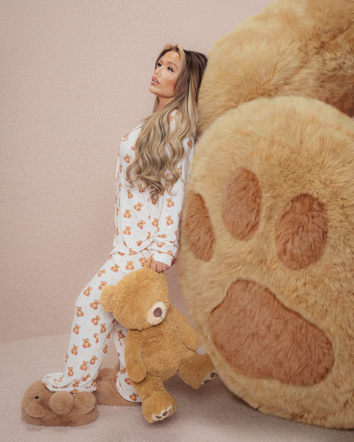 Femme en pyjama en peluche tenant un ours en peluche à côté d'une grande patte d'ours en peluche sur fond beige